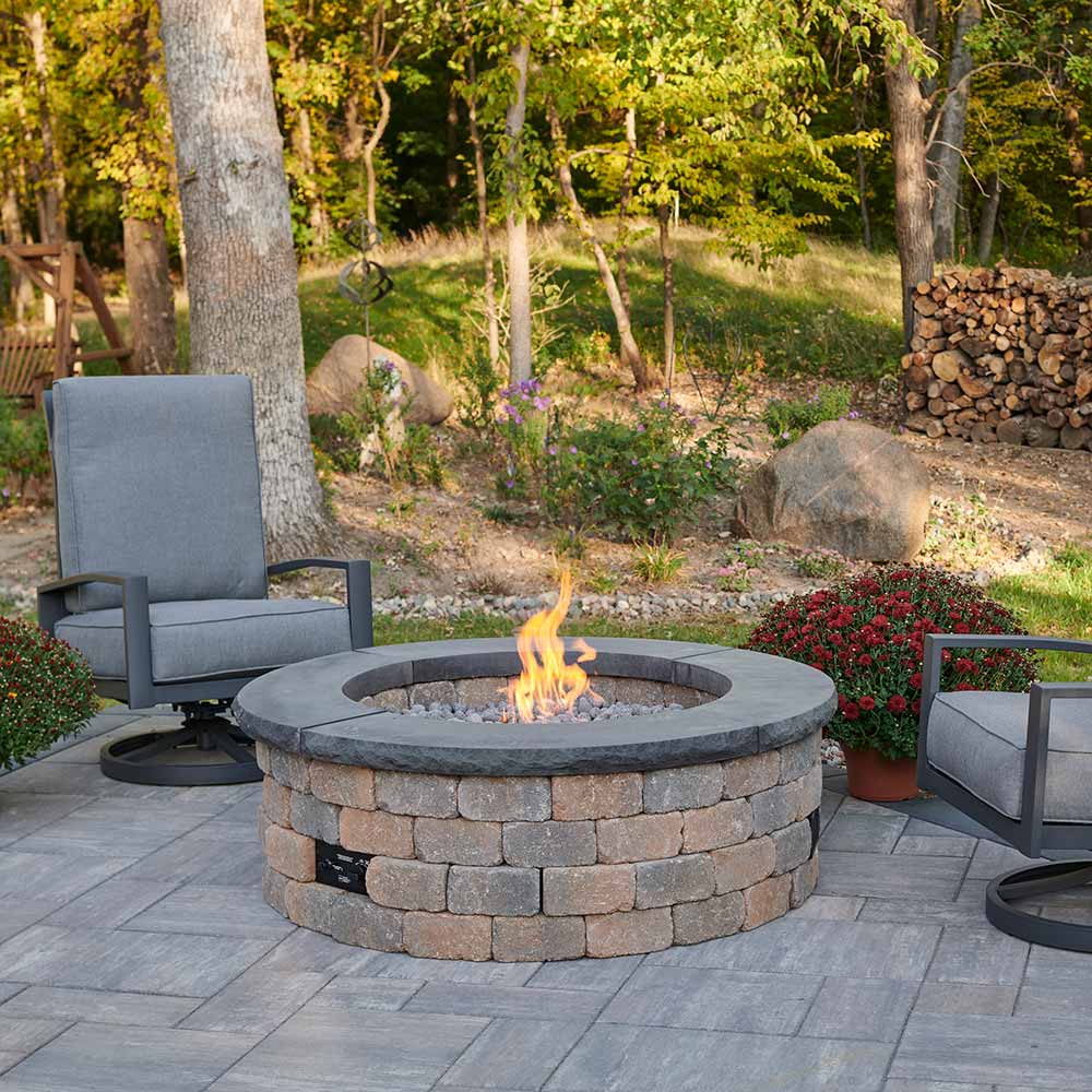 Outdoor round gas fire pit with stone block ring, burning flame, and lava rocks