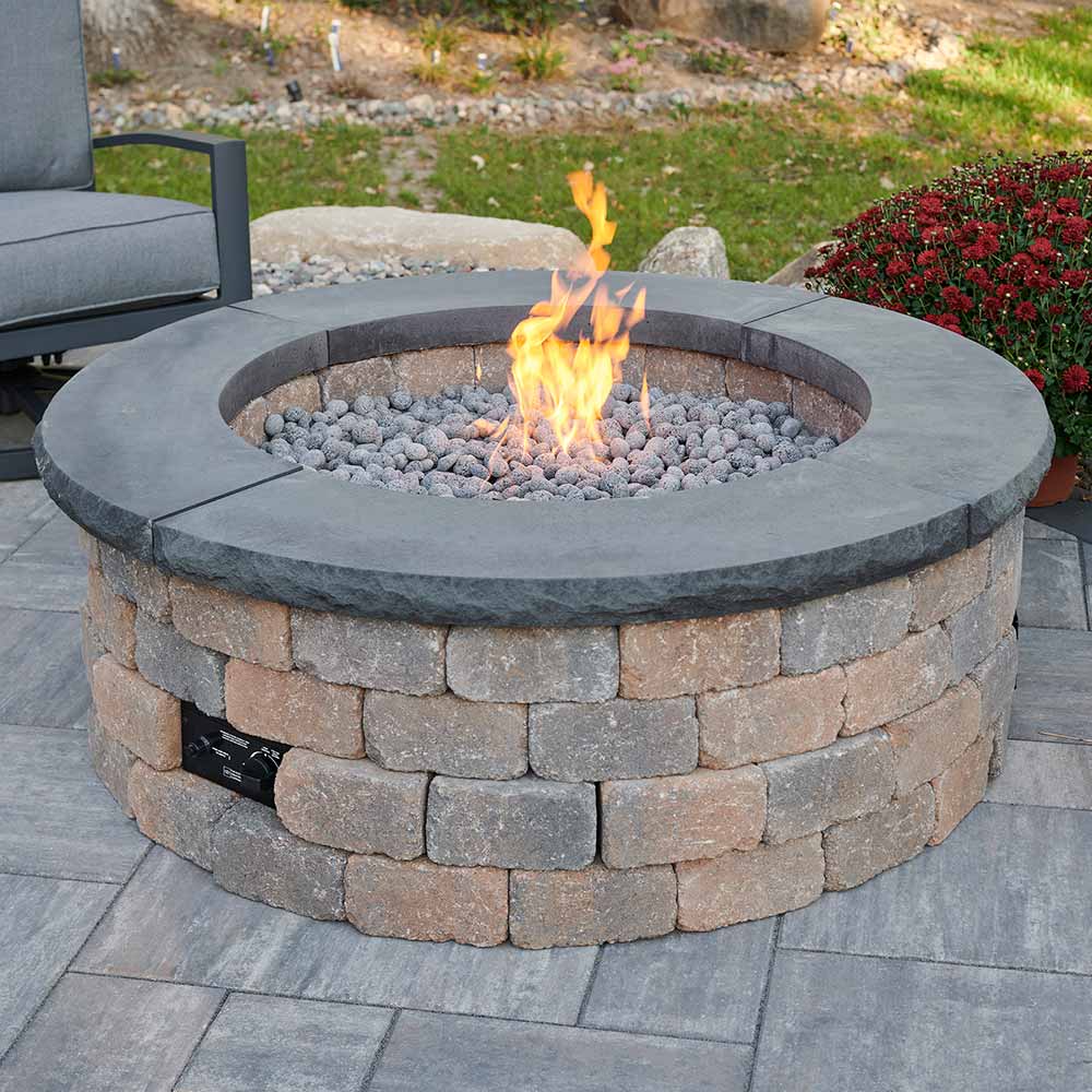 Round gas fire pit kit with stone block ring, burning flame, and lava rocks