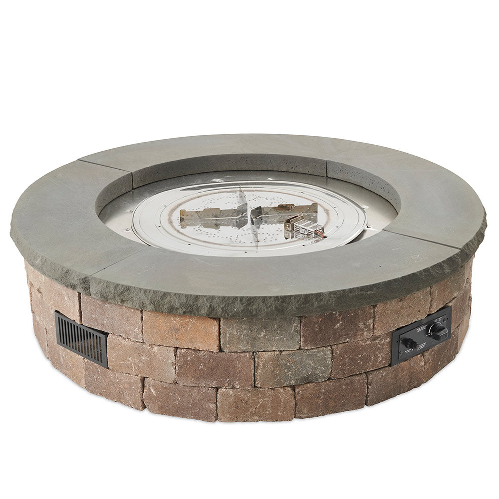 Round gas fire pit kit with open burner pan, stone block ring, and burning flame over rocks