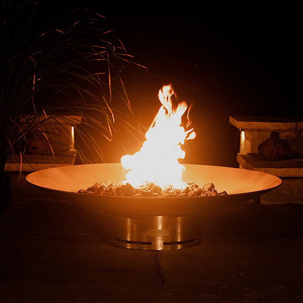 Round stainless steel gas fire pit with flames rising from lava rocks