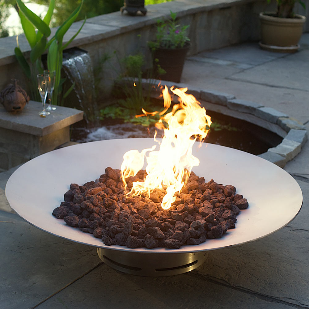 Stainless steel gas fire pit with flames over dark lava rocks in round top