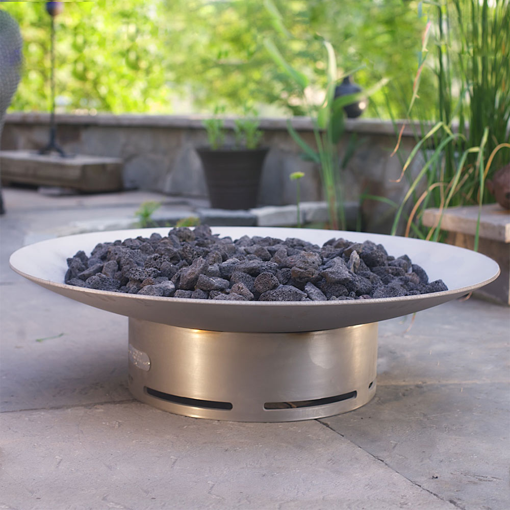 Stainless steel gas fire pit with dark lava rocks on round top, flames not visible
