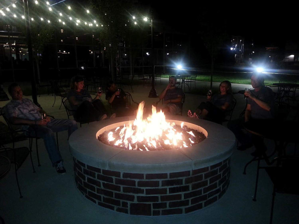 Gas fire pit with round burner and visible flames in a brick base ring