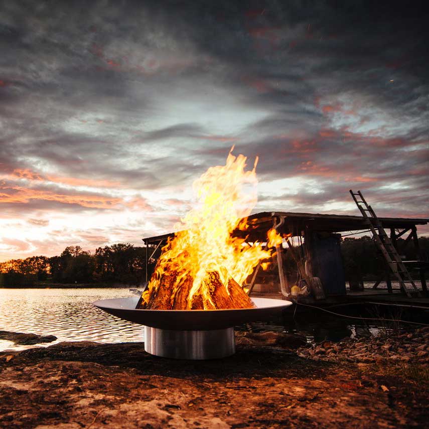 Wood fire pit with tall flames and burning logs in round stainless bowl