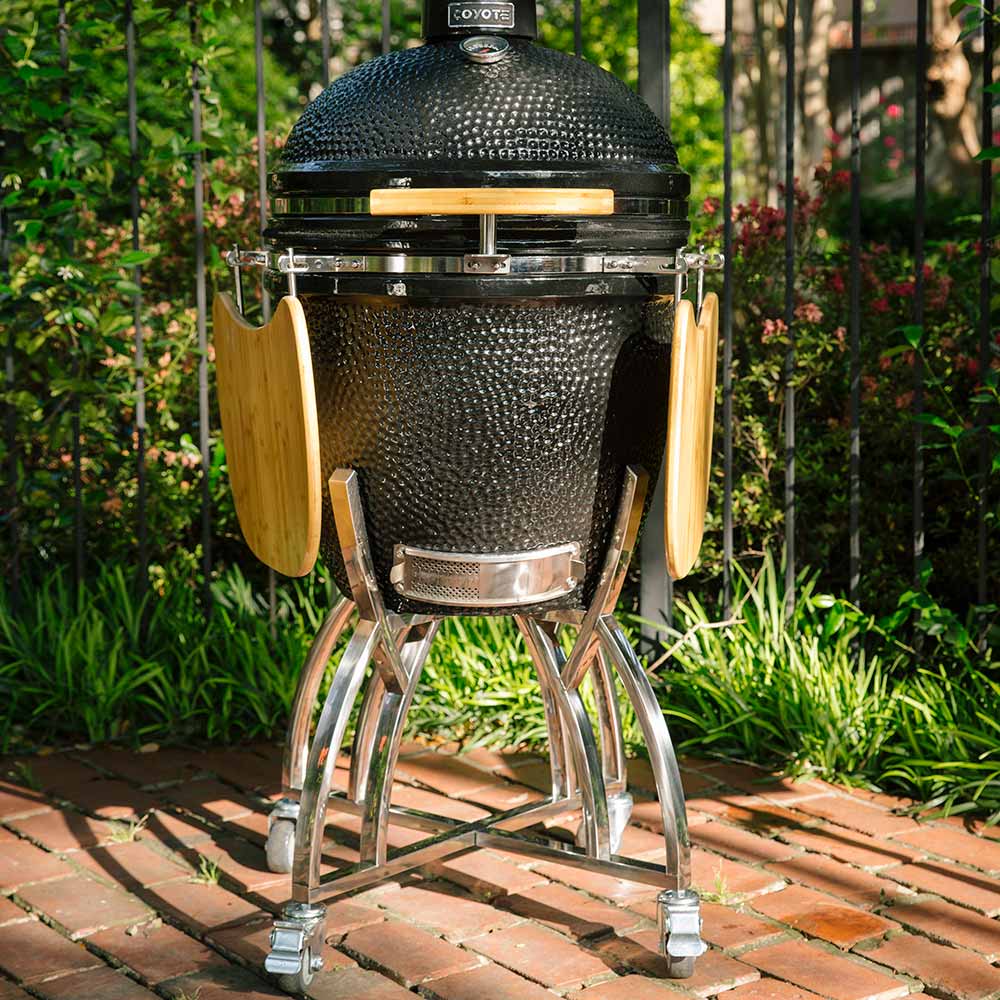 Kamado-style grill stand with wooden side shelves, chrome wheeled base, black textured ceramic