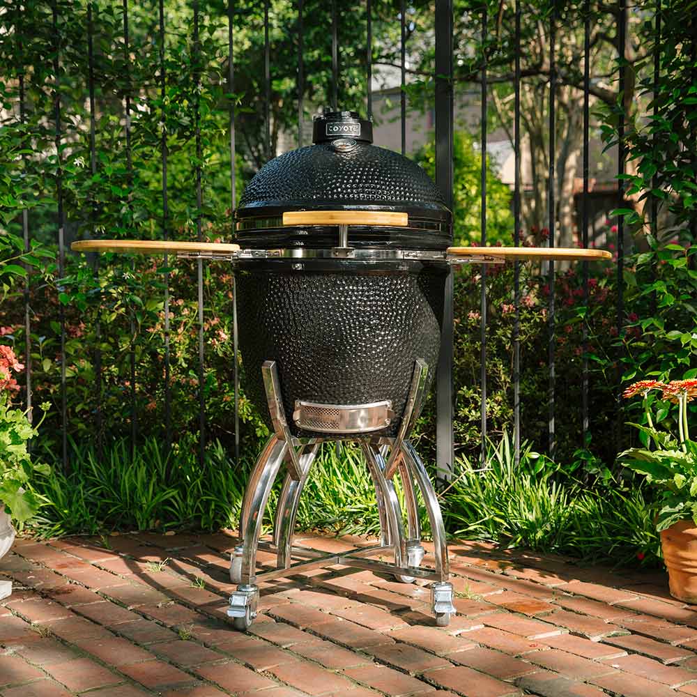 Kamado-style grill with wooden side shelves, black textured dome lid, chrome legs