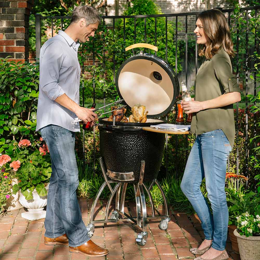 Coyote kamado grill stand with wooden side shelves and open lid, black ceramic body, wheeled base