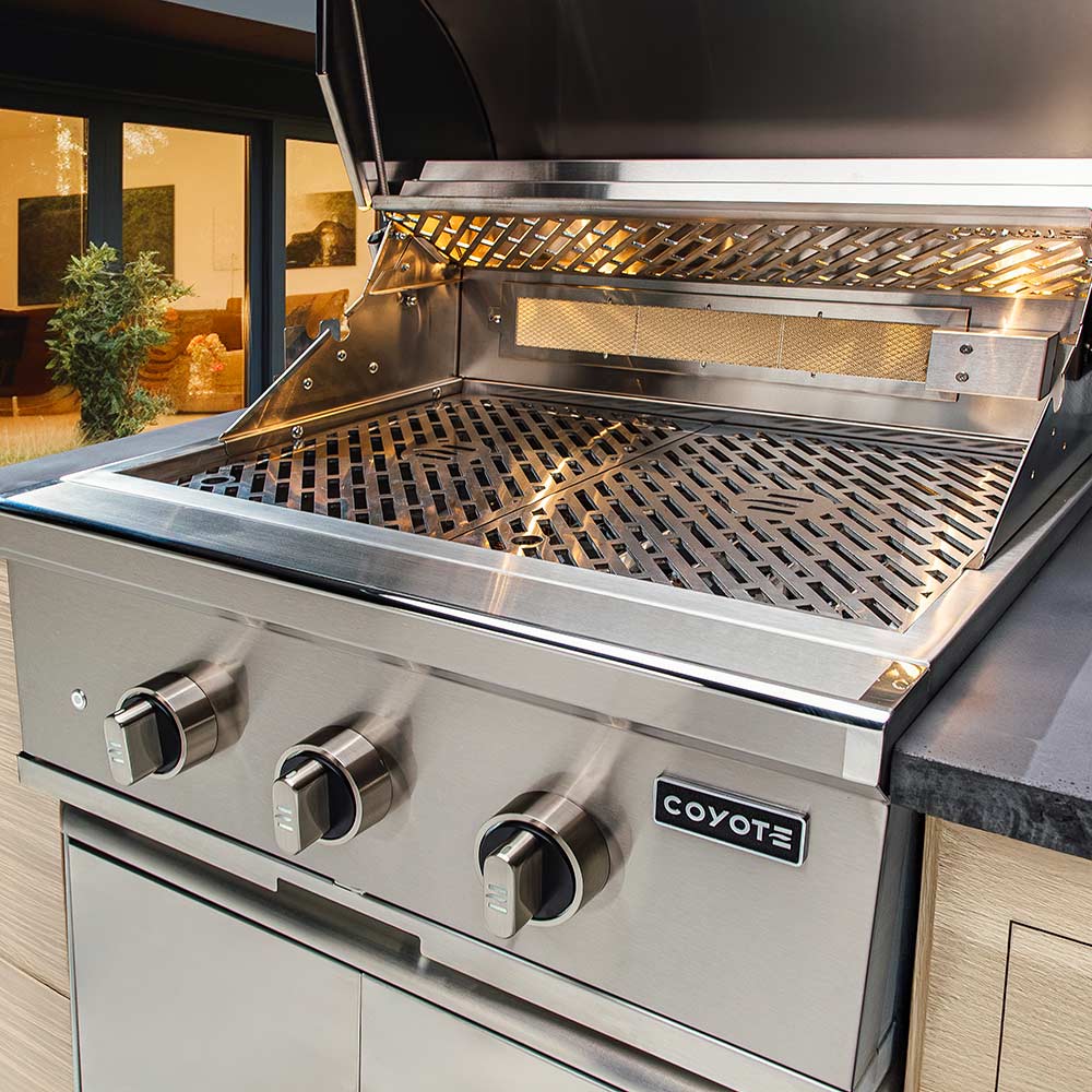 Stainless steel Coyote grill with three control knobs in an outdoor kitchen setting.