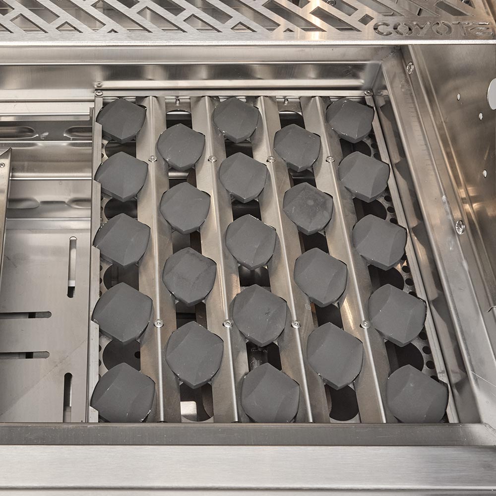 Gas grill burner tray with multiple octagonal burner caps under the stainless hood.