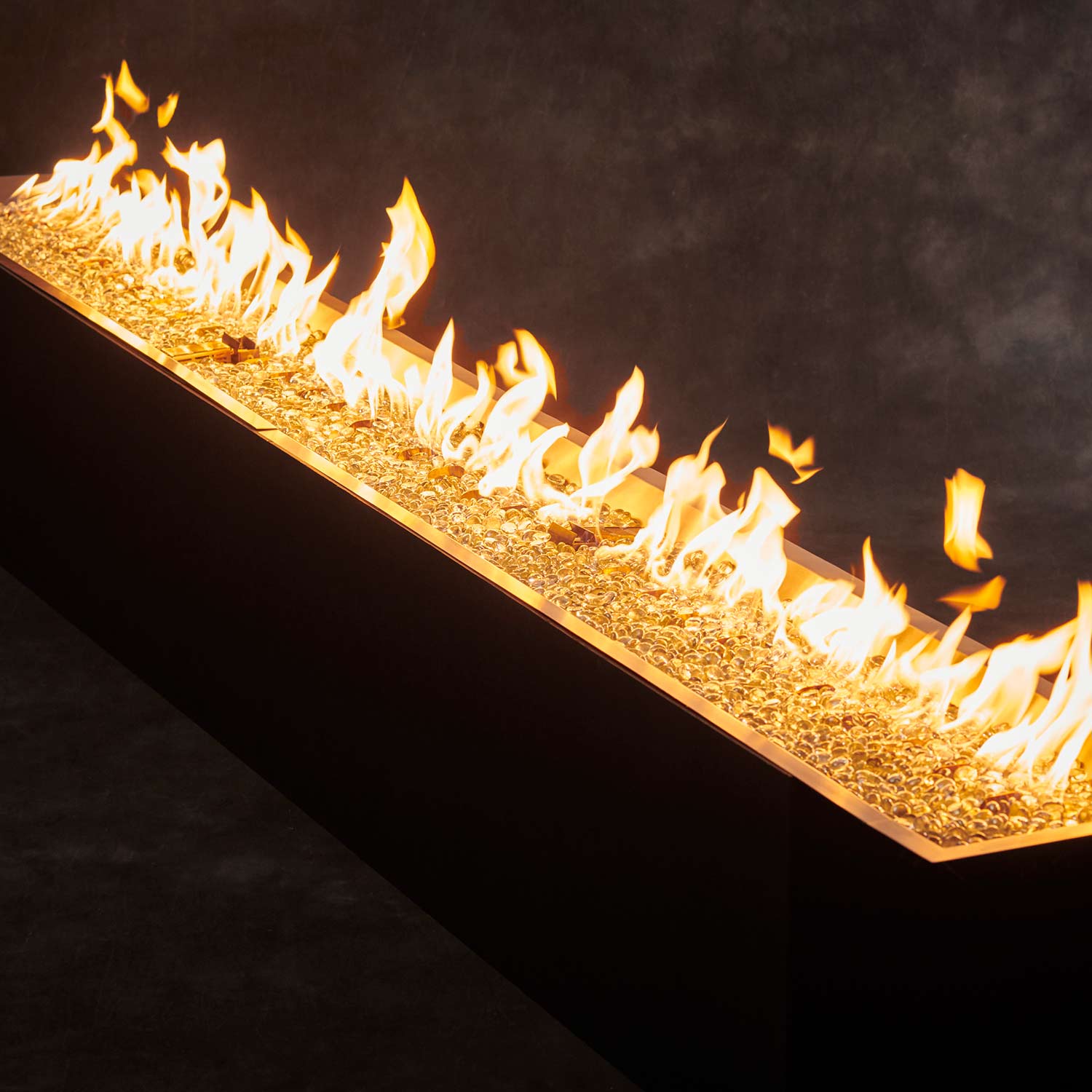 Linear crystal fire pit burner with visible flame jets along the tray
