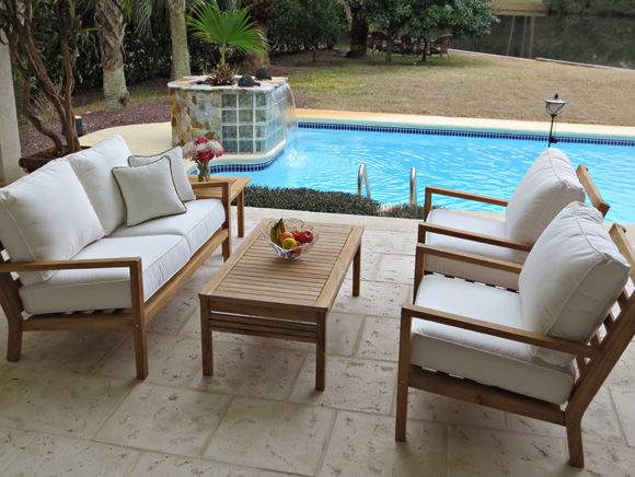 Teak seating loveseat with light cushions and square throw pillows near outdoor pool