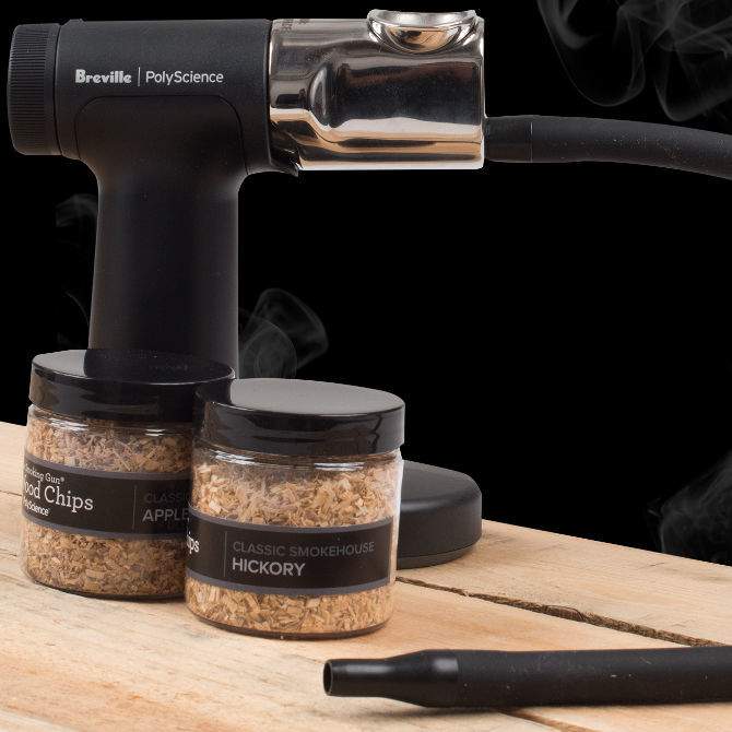 Breville PolyScience smoking device with jars of wood chips on a wooden surface