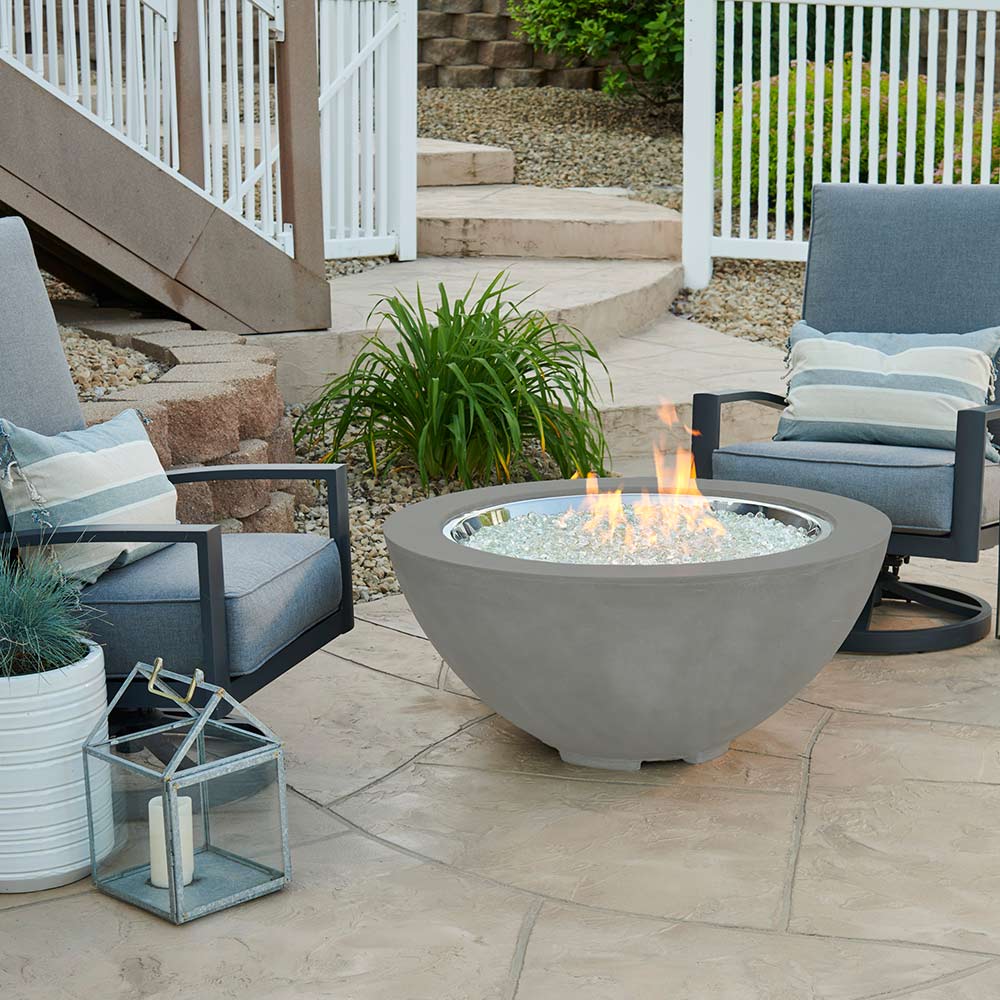 Grey gas fire pit bowl burning with visible flame over glass burner media