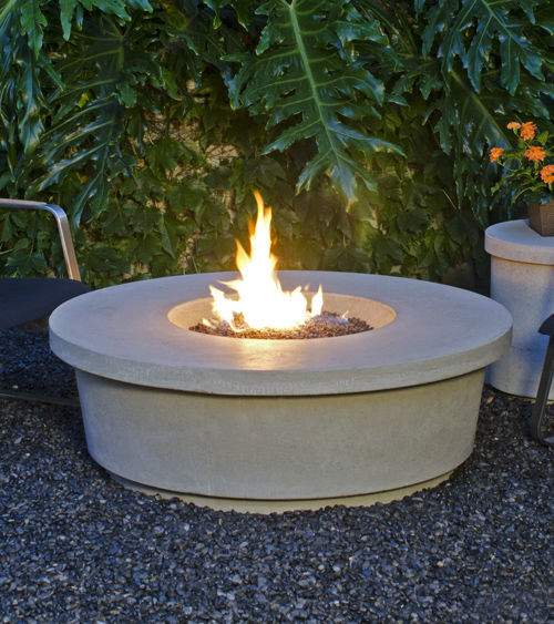 Round GFRC fire table with active flame, light gray fire bowl on patio.