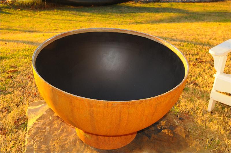 Orange metal fire pit bowl with dark interior basin on outdoor ground
