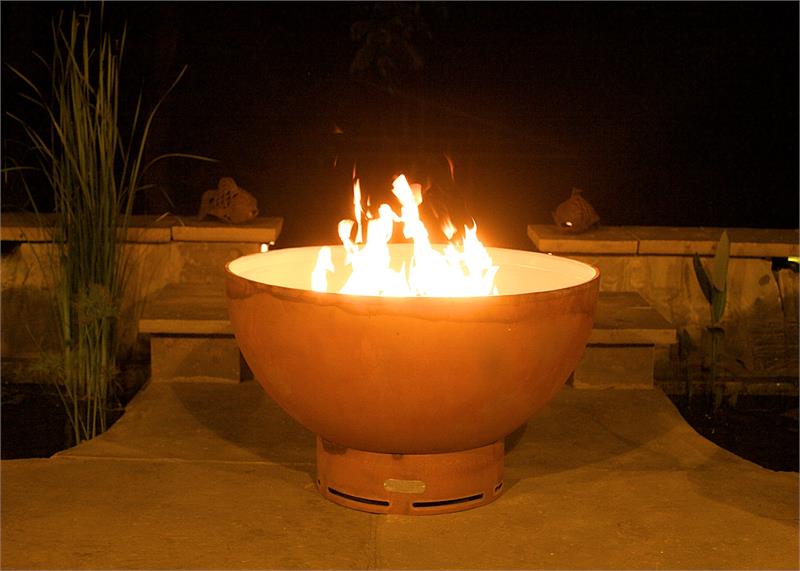 Orange metal wood fire pit with flames rising from center on stone base
