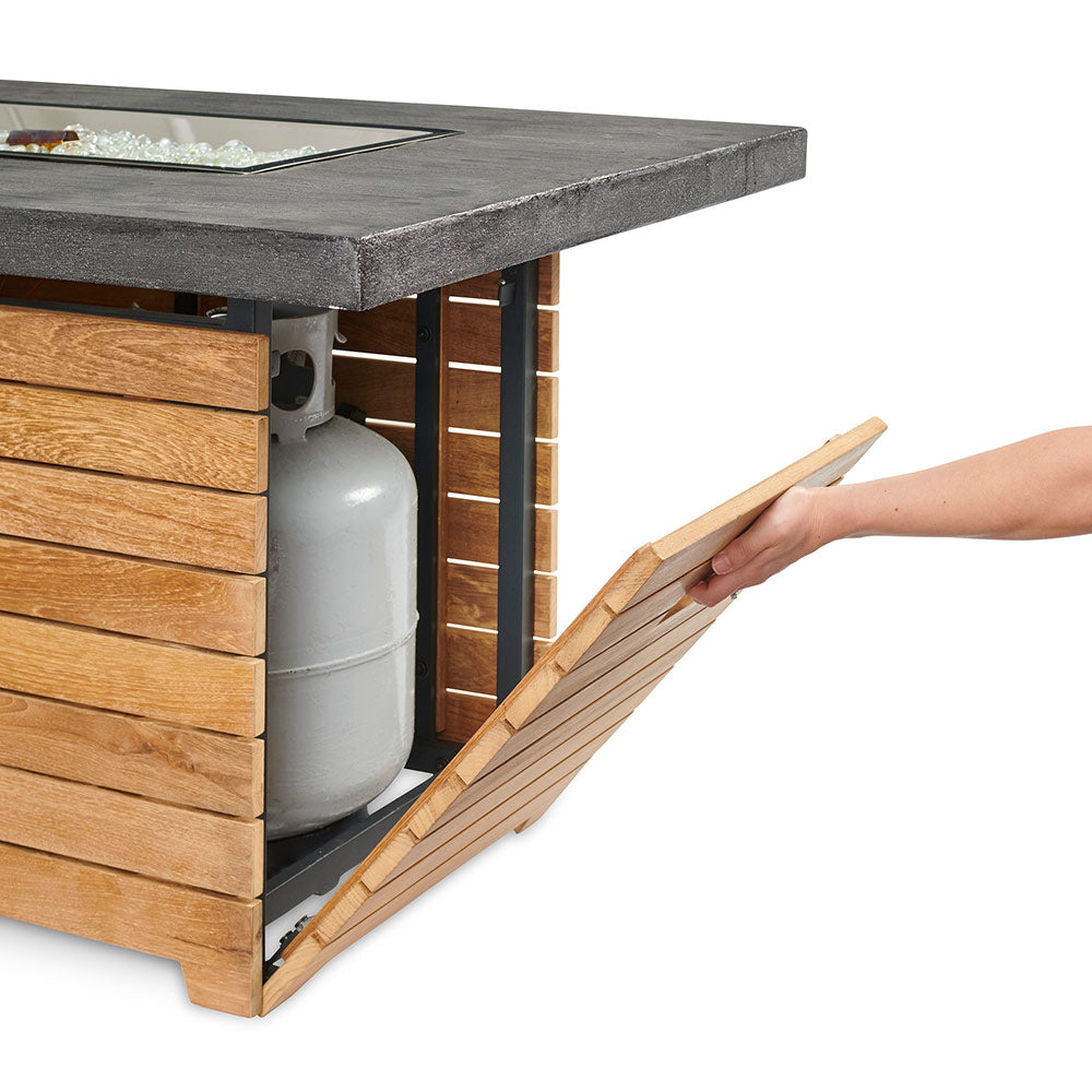 Outdoor gas fire pit table with dark top and teak base, side access panel with fuel tank