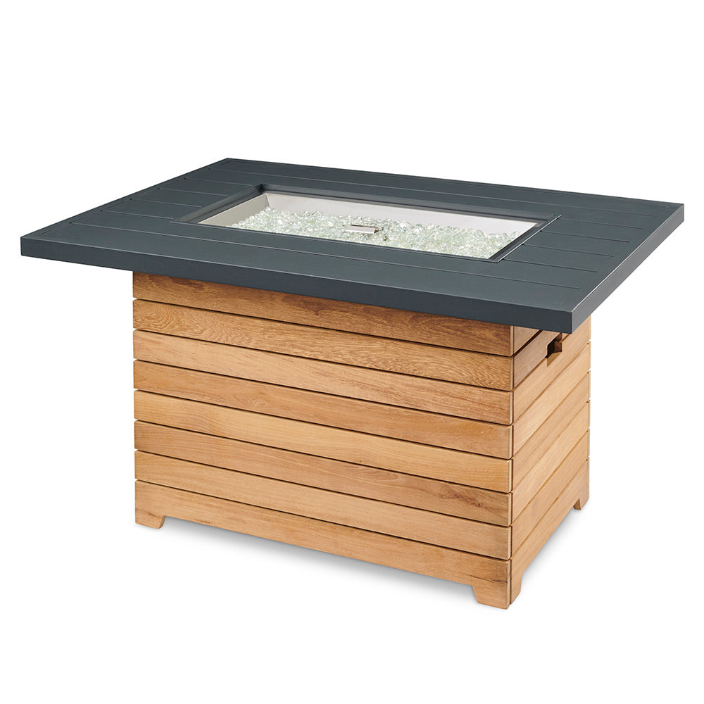 Gas fire pit table with dark aluminum top and teak wood base, glowing burner bed
