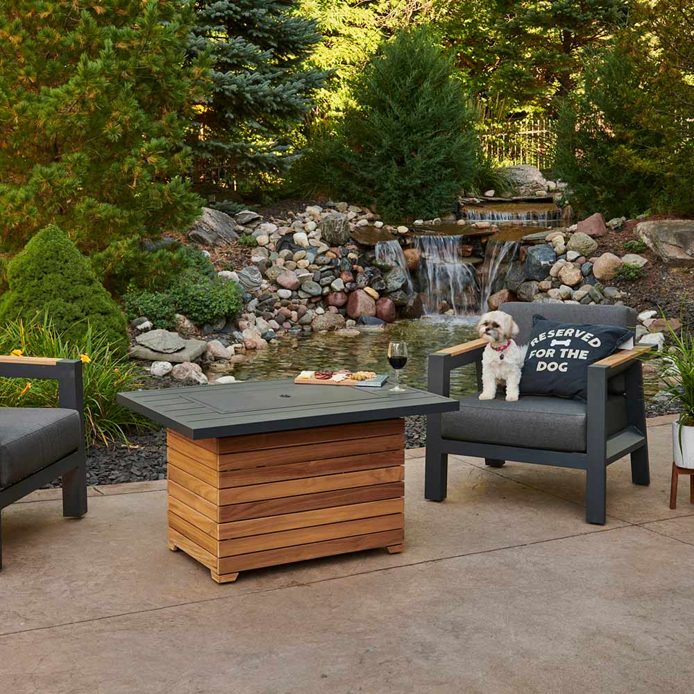 Outdoor gas fire pit table with dark aluminum top and teak base, flames burning