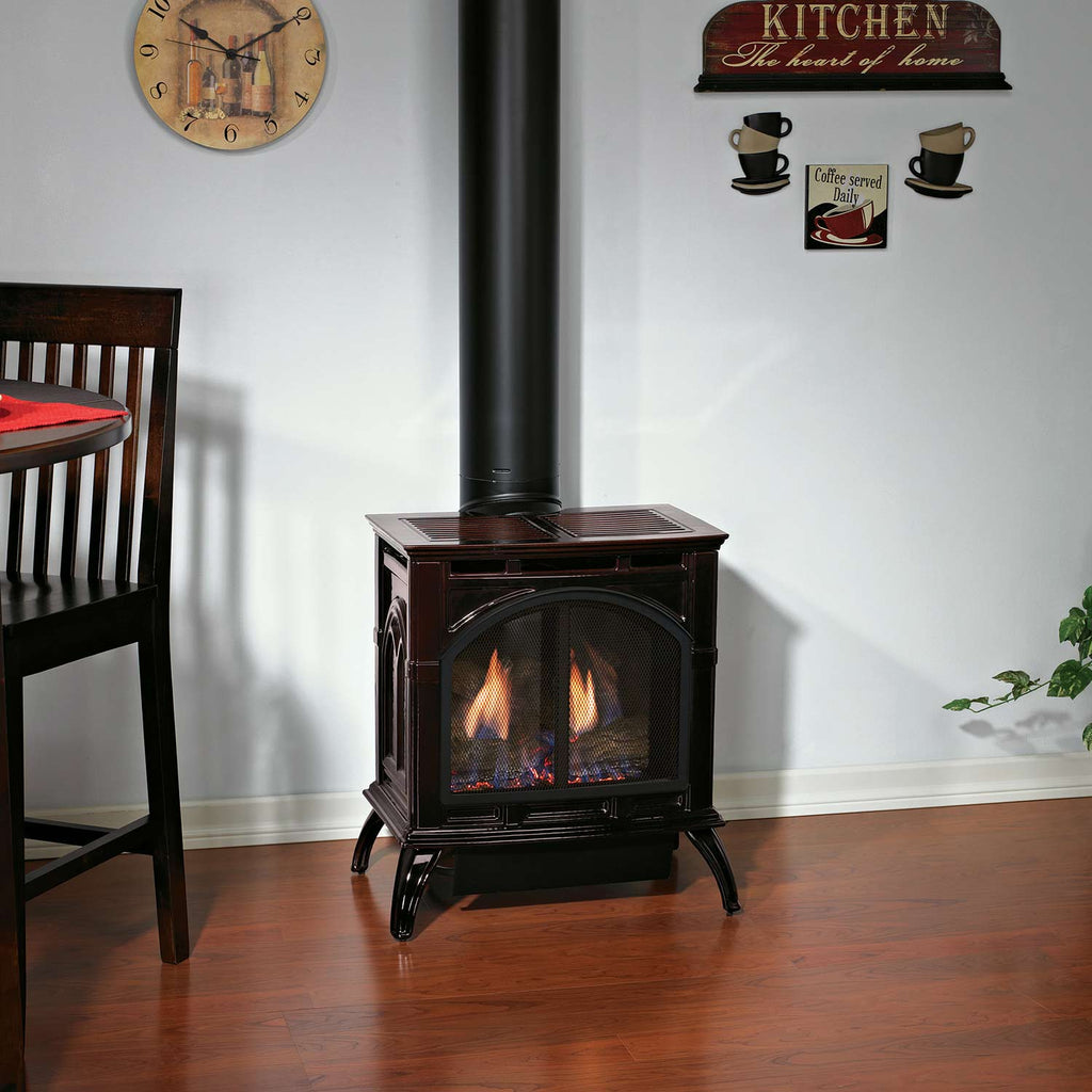 Dark cast iron direct-vent stove with lit glass doors and vertical flue pipe.