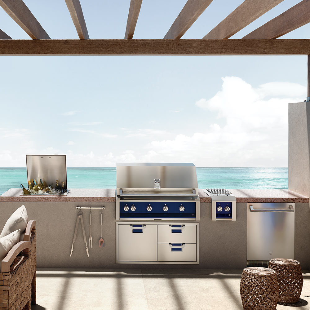 Outdoor built-in gas grill with four burner knobs, side shelf, and cabinet storage.