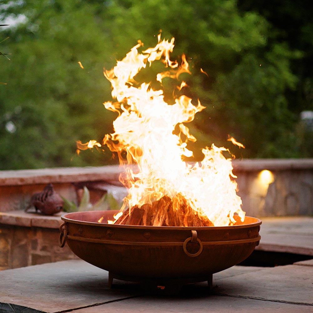 Emperor wood fire pit with flames rising above bronze rim on patio