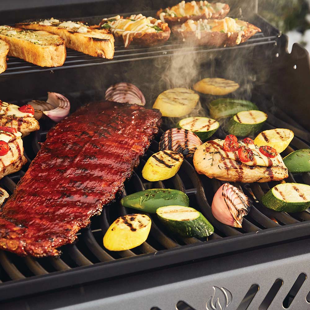 Freestyle 365 gas grill with lid open, steaks and sliced vegetables on grates