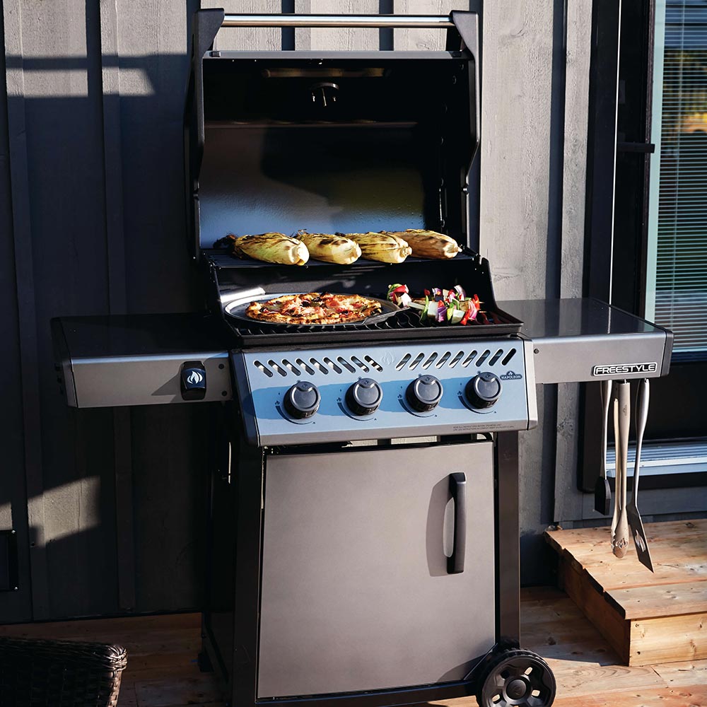 Gas grill with open lid, food on cooking surface and side shelf, black