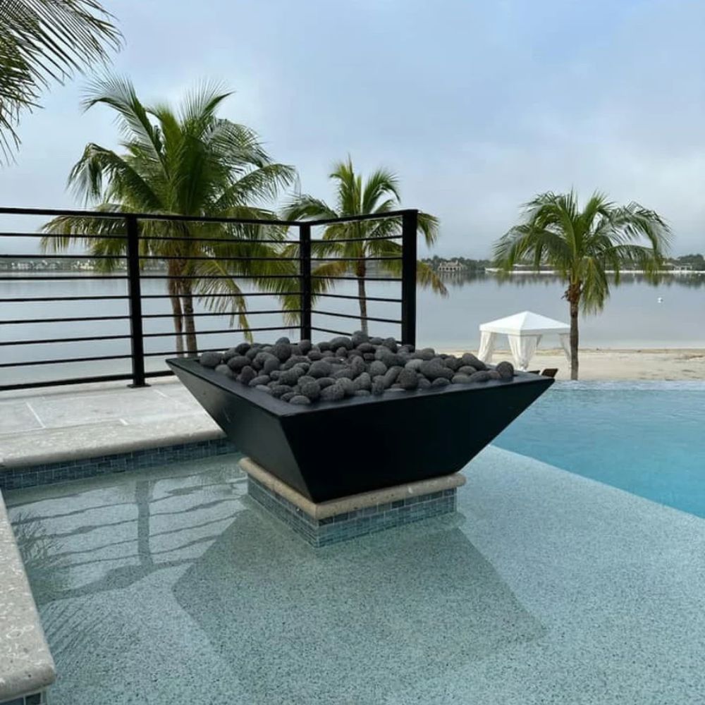 Concrete gas fire bowl with flame and dark stones inside, set within a water feature