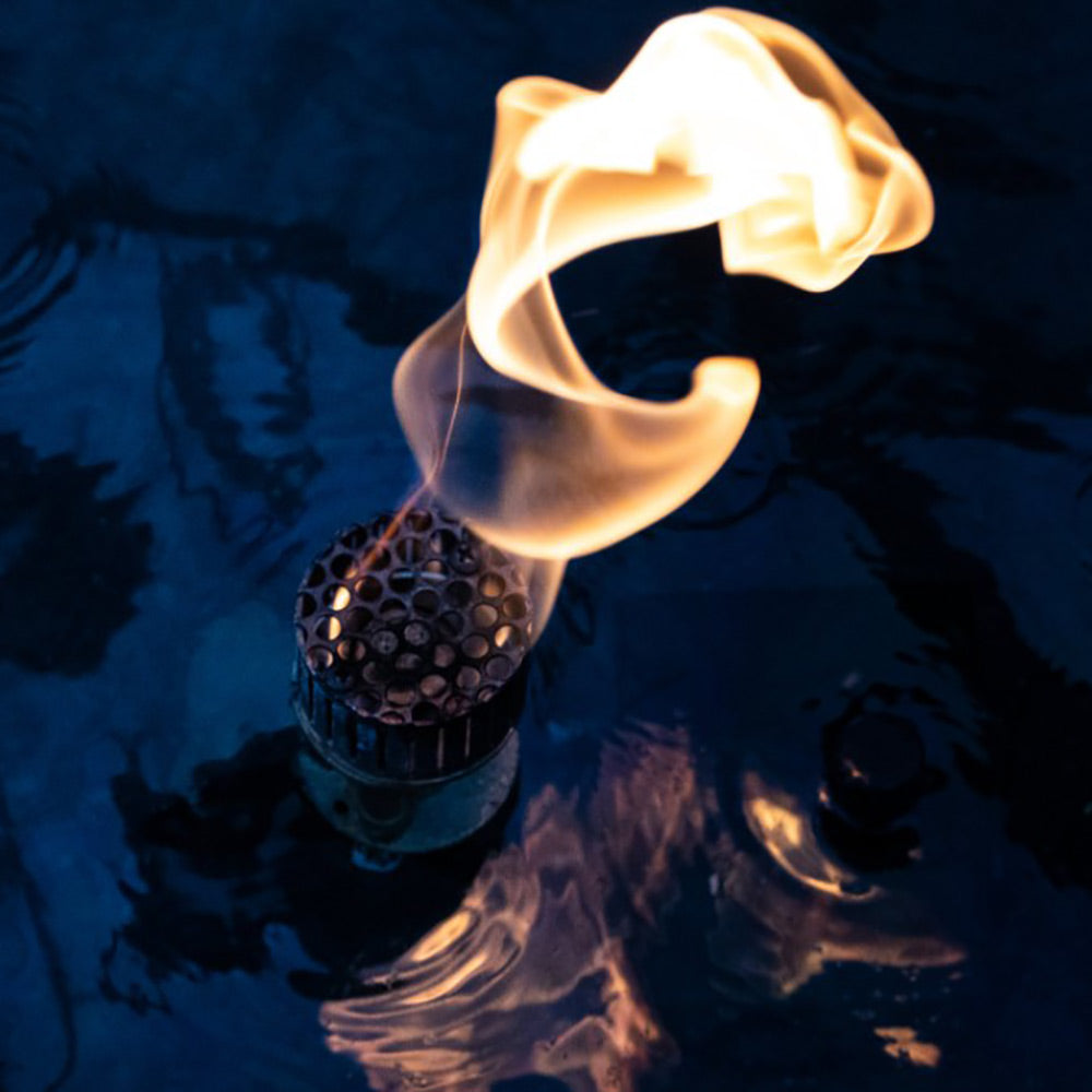 Flame curls from a metal burner over water, with blue reflections