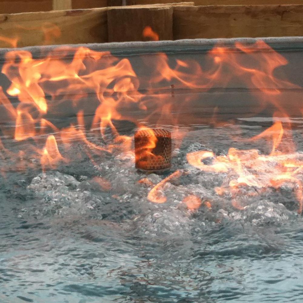 Flame rising over water in a fire bowl, with glowing embers