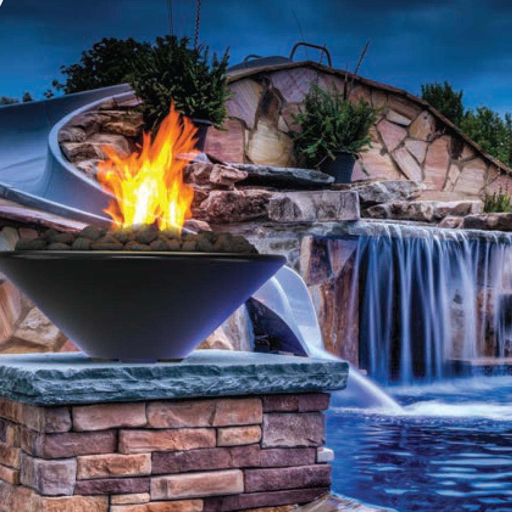 Dark gray concrete gas fire bowl with visible flames, set on a stone outdoor base