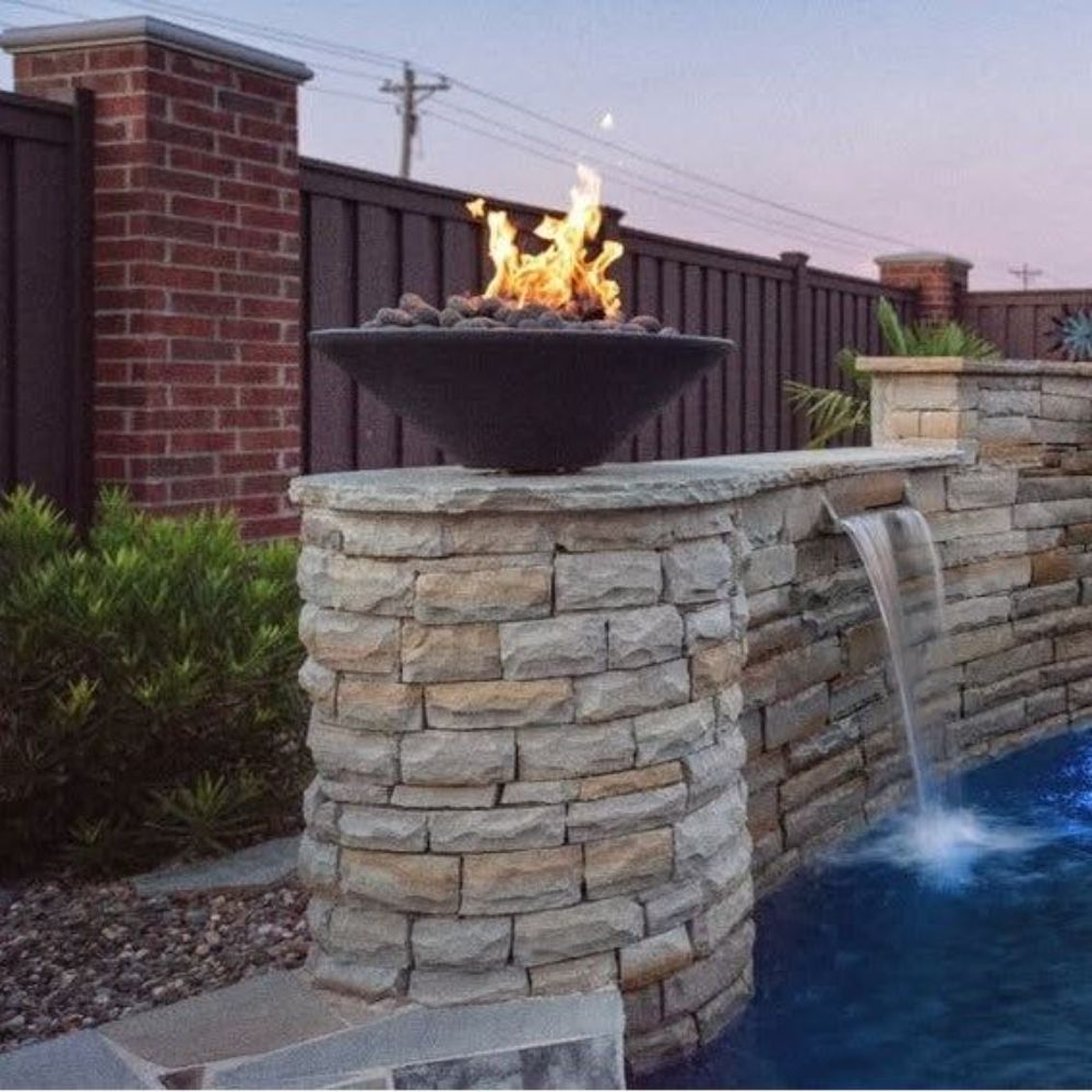 Dark gray concrete gas fire bowl mounted on a stone column, with flames visible