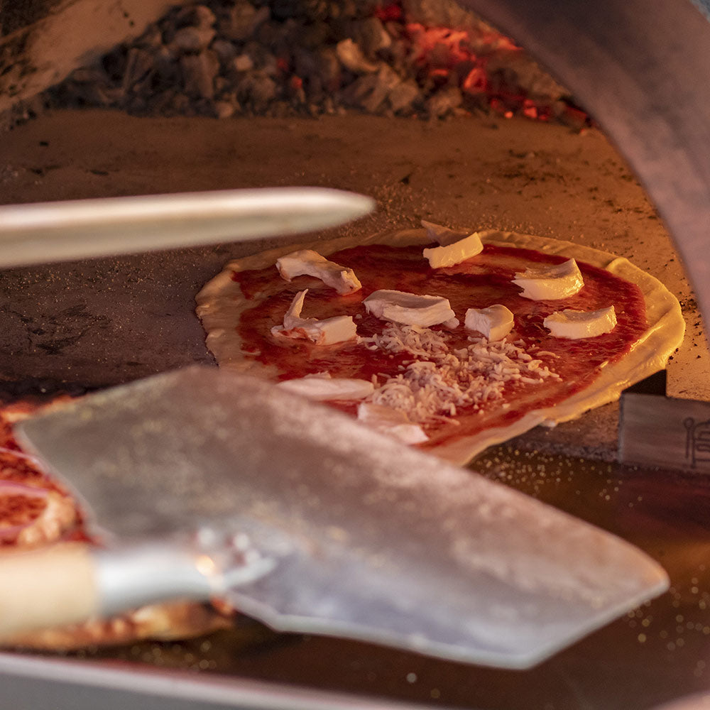 Aluminum pizza peel lifting a topped pizza from a hot oven hearth