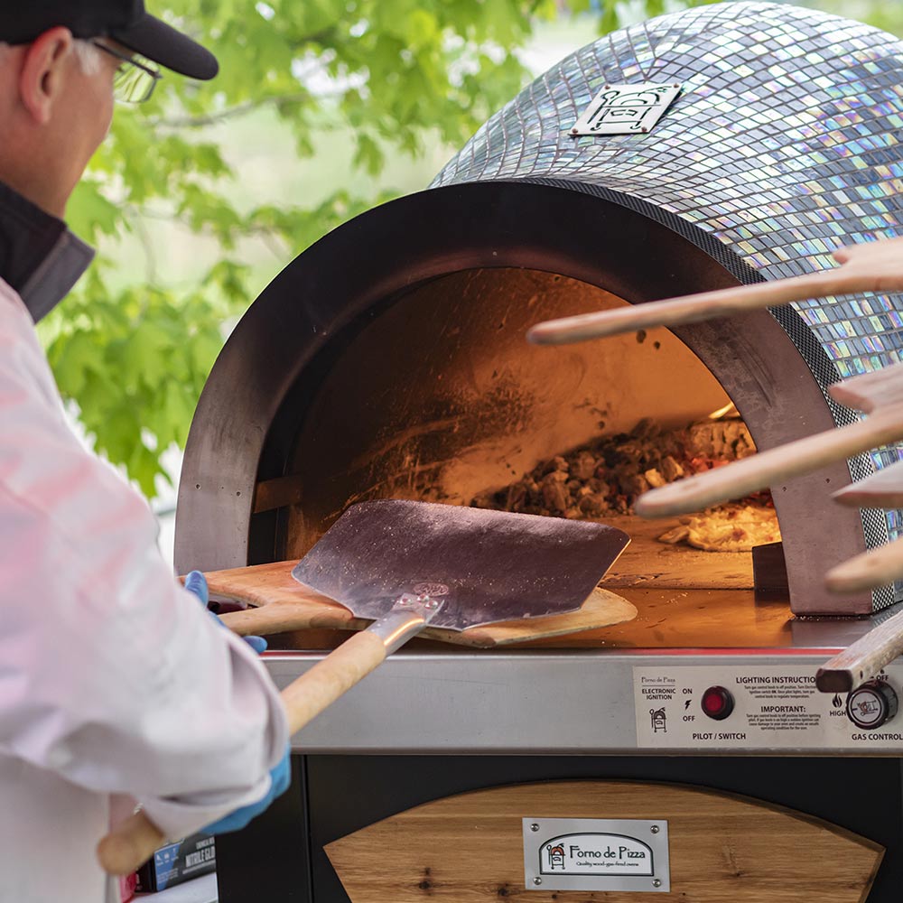 Aluminum pizza peel being used inside a wood-fired oven to slide pizzas
