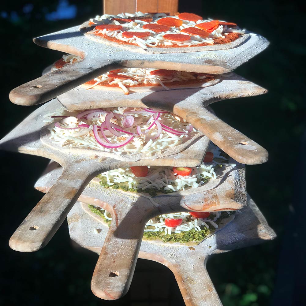 Wooden pizza paddle lifting a topped pizza over a grill