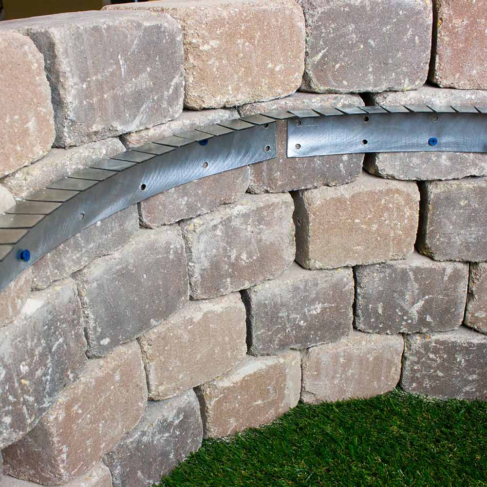 Flexible metal installation collar fitted around a stone wall corner with blue bolt heads