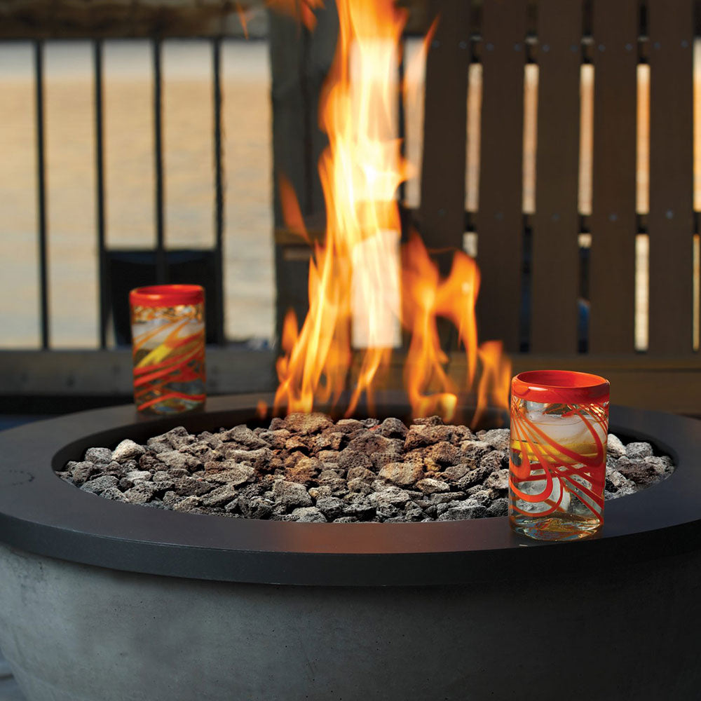 Round gas fire pit burner with black rim and tall flame over lava rocks