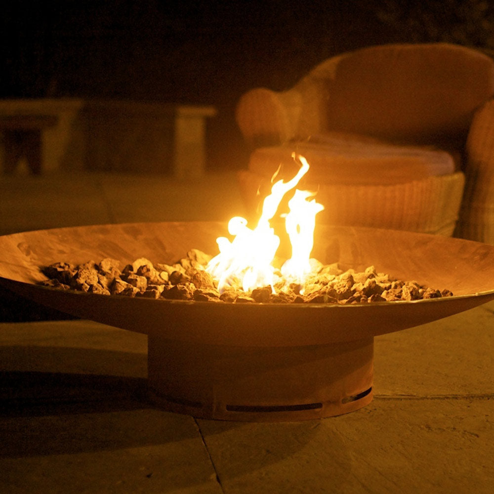 Gas fire pit with flame in round metal bowl and glowing lava rock burner bed