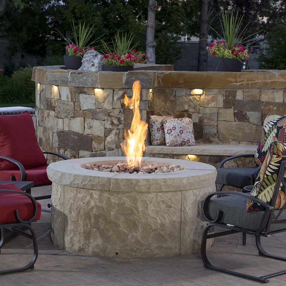 Round outdoor gas fire pit with flame, stone surround, and fire media