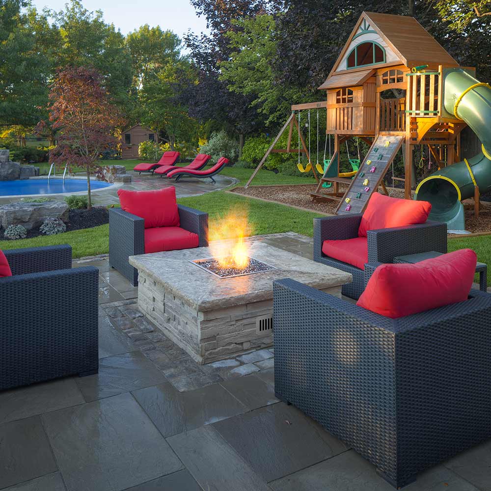 Outdoor patio gas fire pit with visible flame in square stone surround