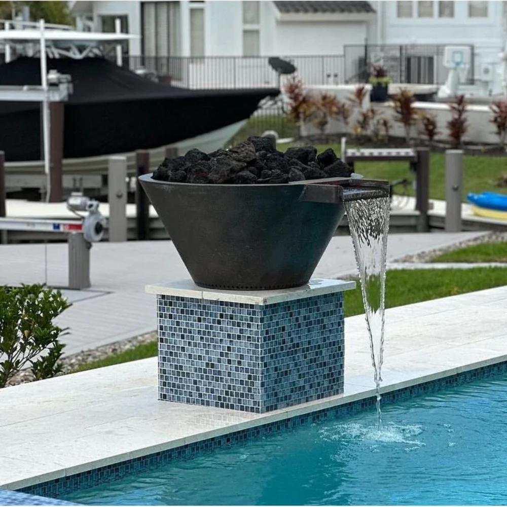 Round gas fire and water bowl on blue mosaic pedestal with rocks and flowing water near a pool