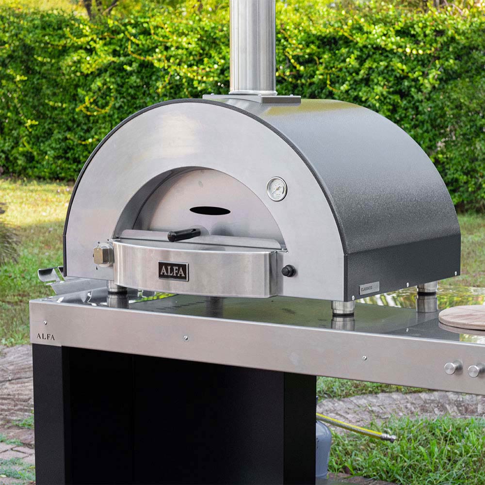Stainless gas pizza oven with closed arched door, chimney stack, and side control knobs.