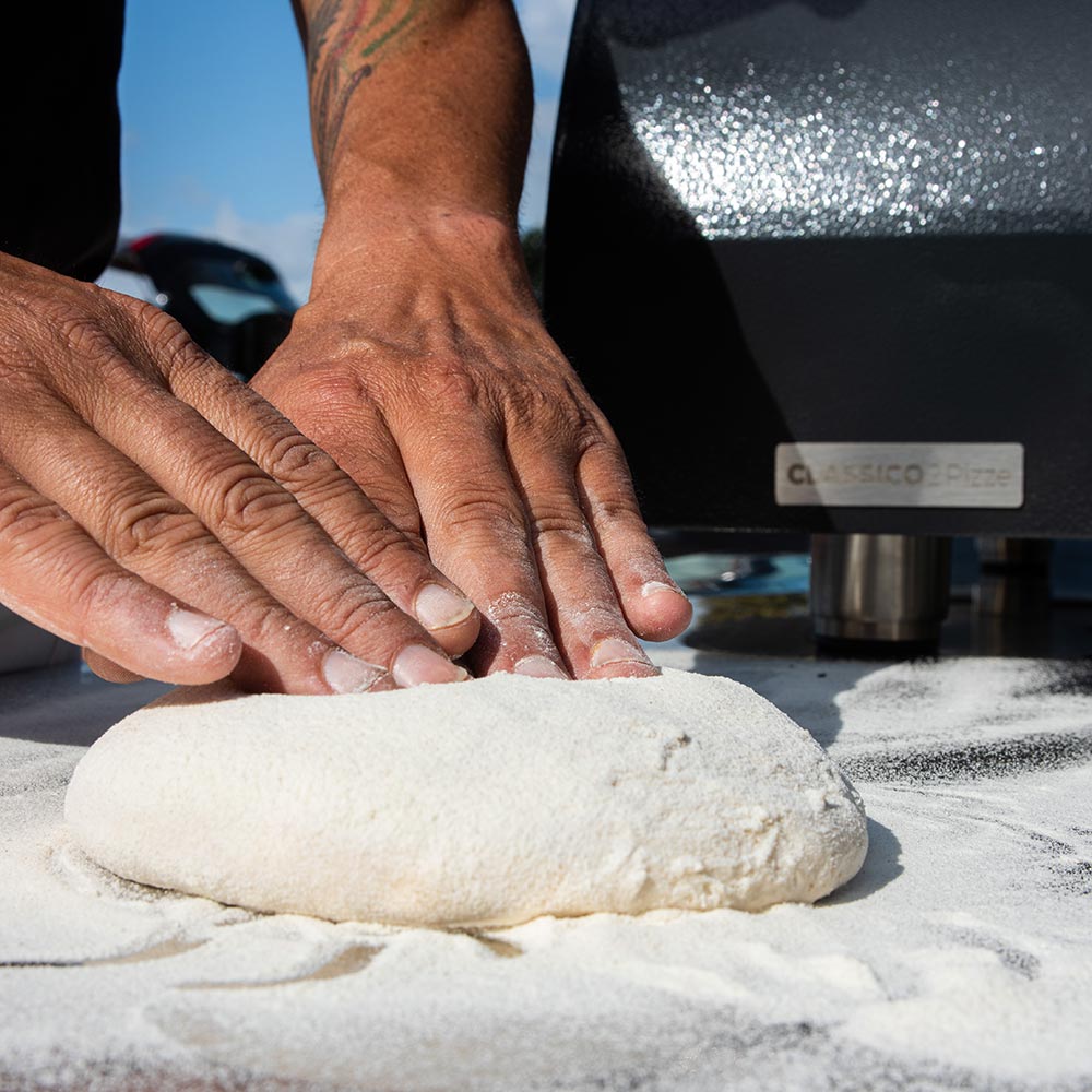 Alfa gas pizza oven in-use: hands top a dough crust on the oven stone