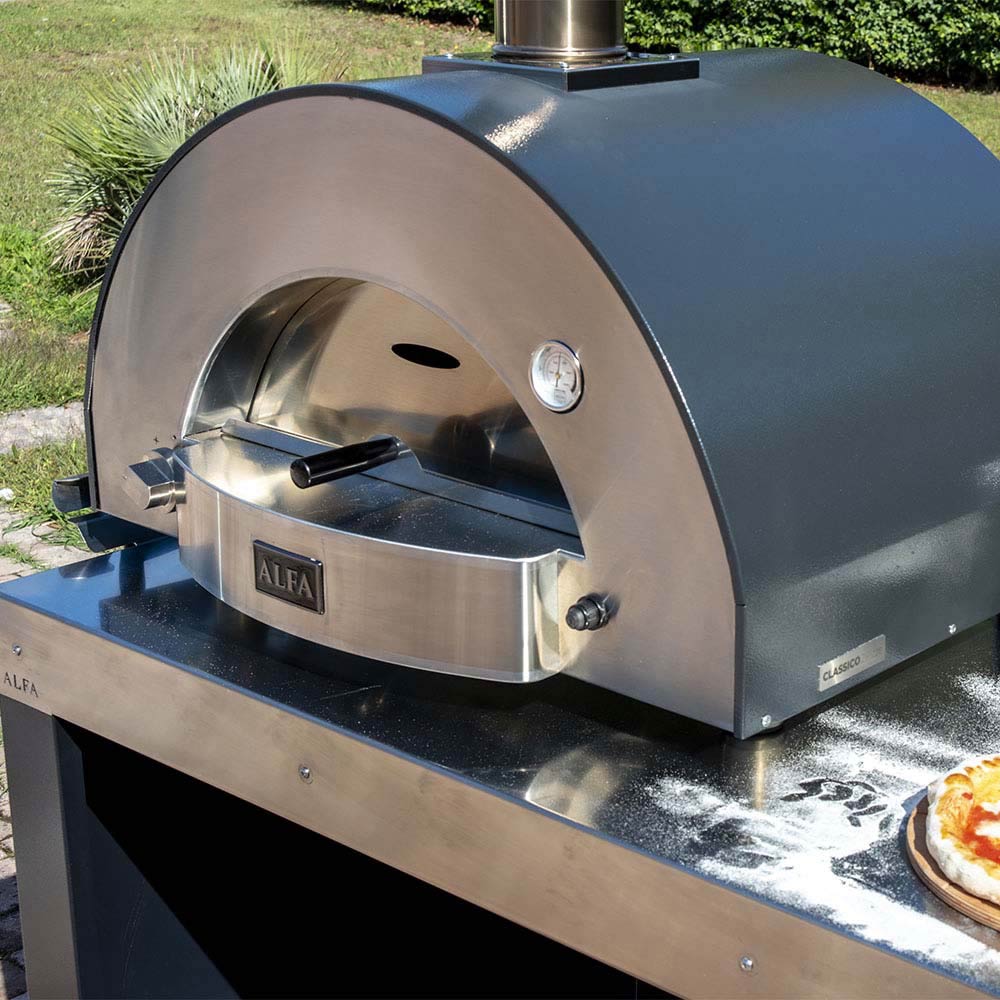 Outdoor wood-fired pizza oven on stainless counter with front control knob and door.