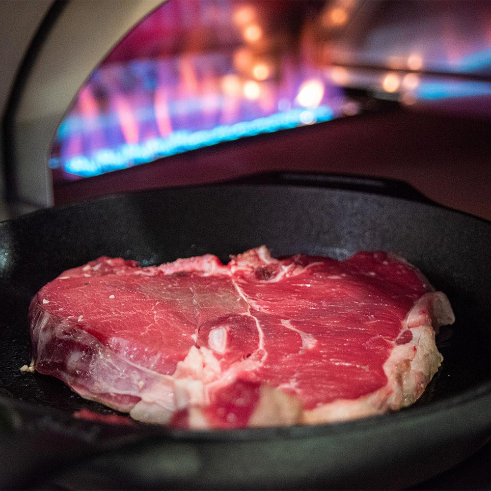 Pizza oven cooking chamber with a steak on the heated stone surface