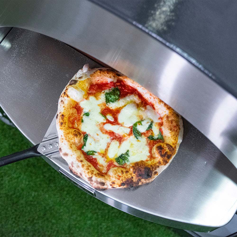 Stone-baked pizza on a metal peel/board beside the open oven dome