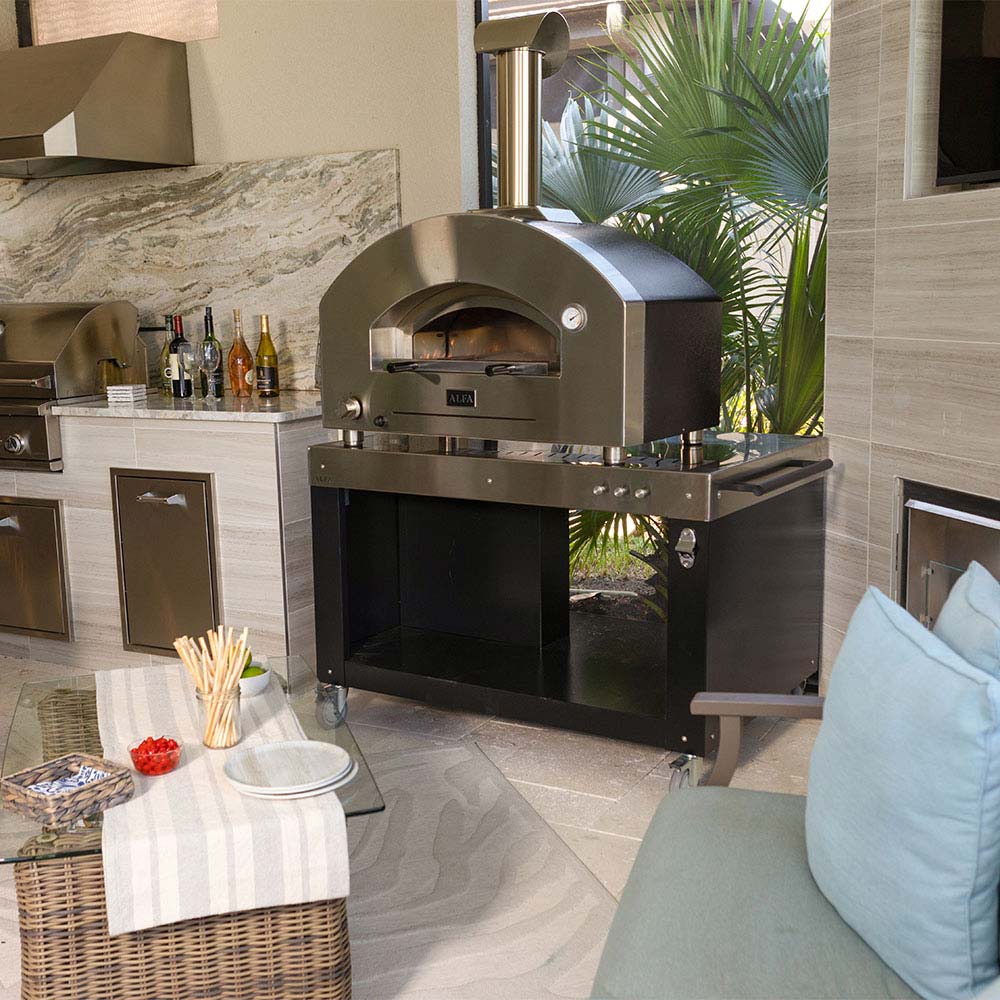 Outdoor pizza oven with open dome, stainless cart and countertop accessories nearby
