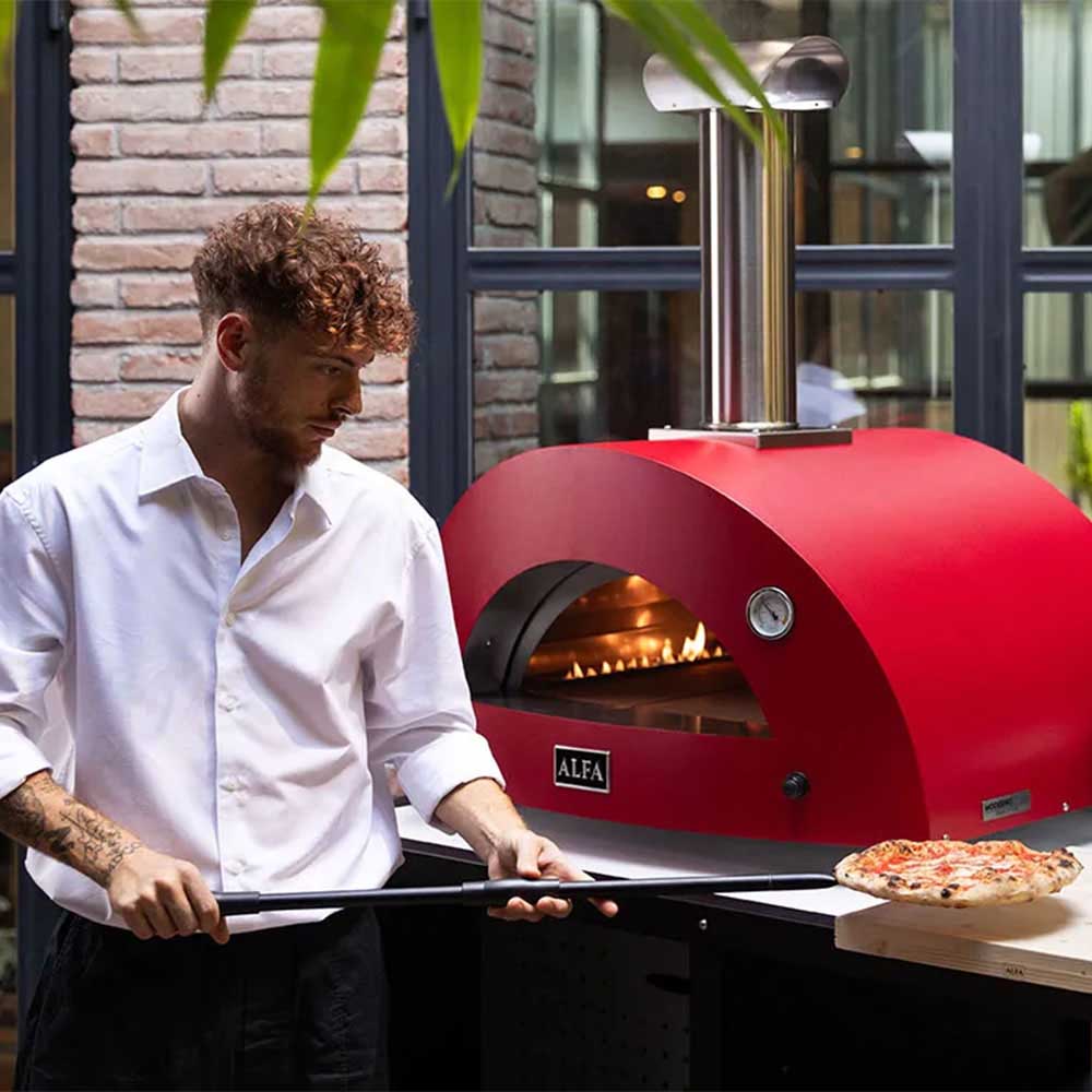 Ruby red countertop gas pizza oven with chef placing a pizza onto the cooking deck.