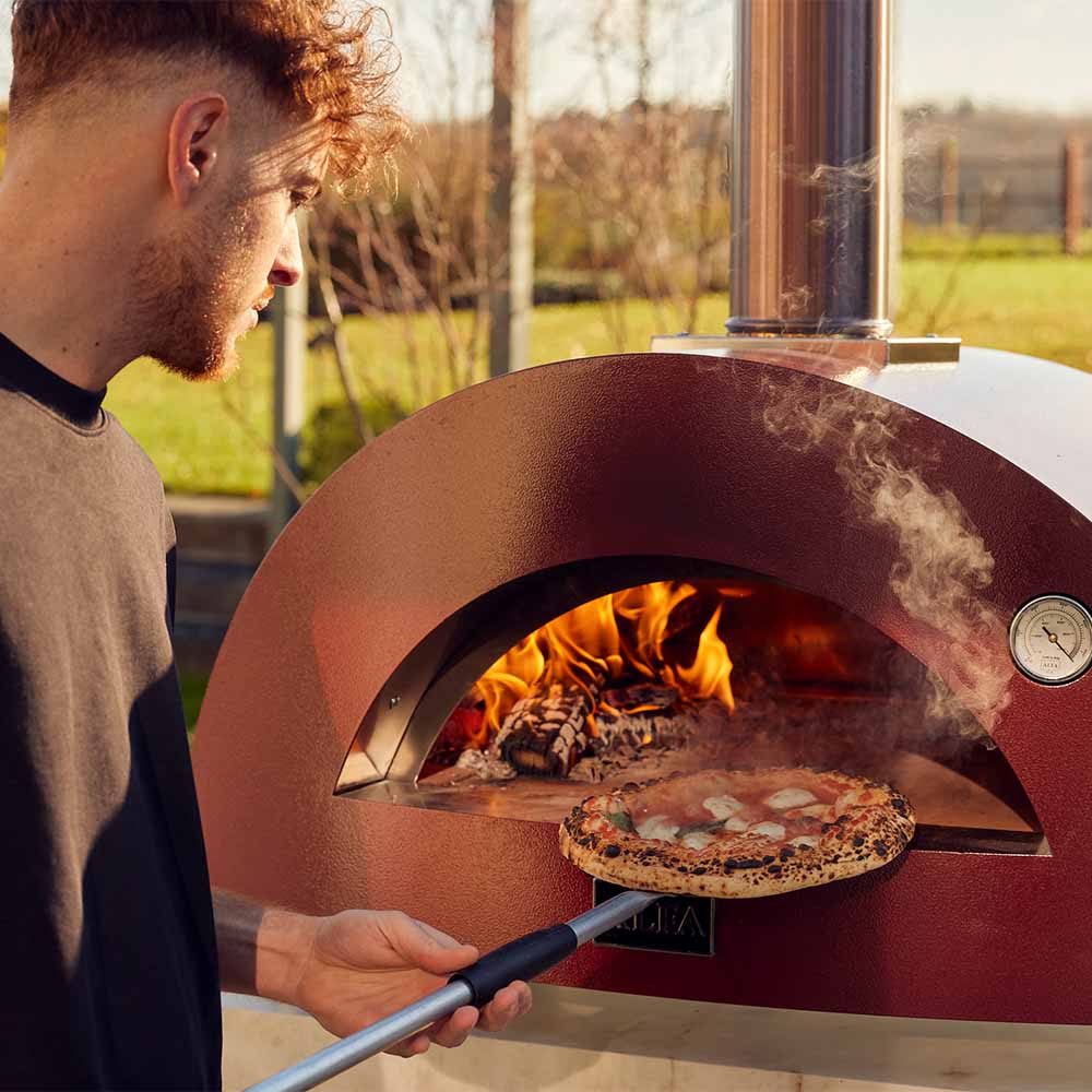 Wood-fired pizza oven with pizza on stone, red dome and open hearth with flames